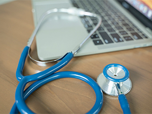 Stethoscope atop a laptop keyboard and light wooden desk
